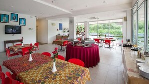 A spacious dining area with multiple tables, red chairs, and a large window providing a view of the outdoors. - Syajie Koptown Hotel (Segamat)