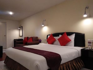 A hotel room with a large bed, two bedside lamps, a nightstand, and a chair.