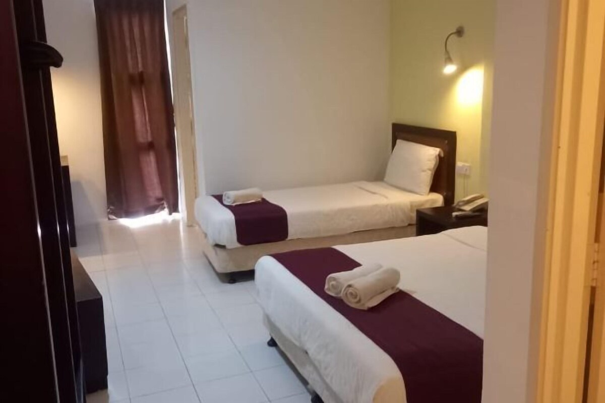 Habitación de hotel con dos camas, una mesita de noche, una lámpara y una puerta que da a otra habitación.