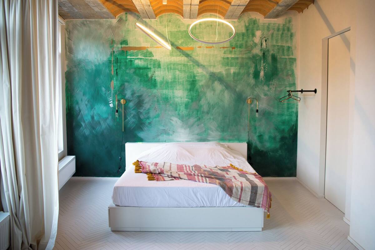 A bedroom with a bed, a green textured wall, and a white floor.