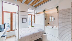 A modern bedroom with a bed, a desk, a TV, and a large window. - The Hide (Ghent)