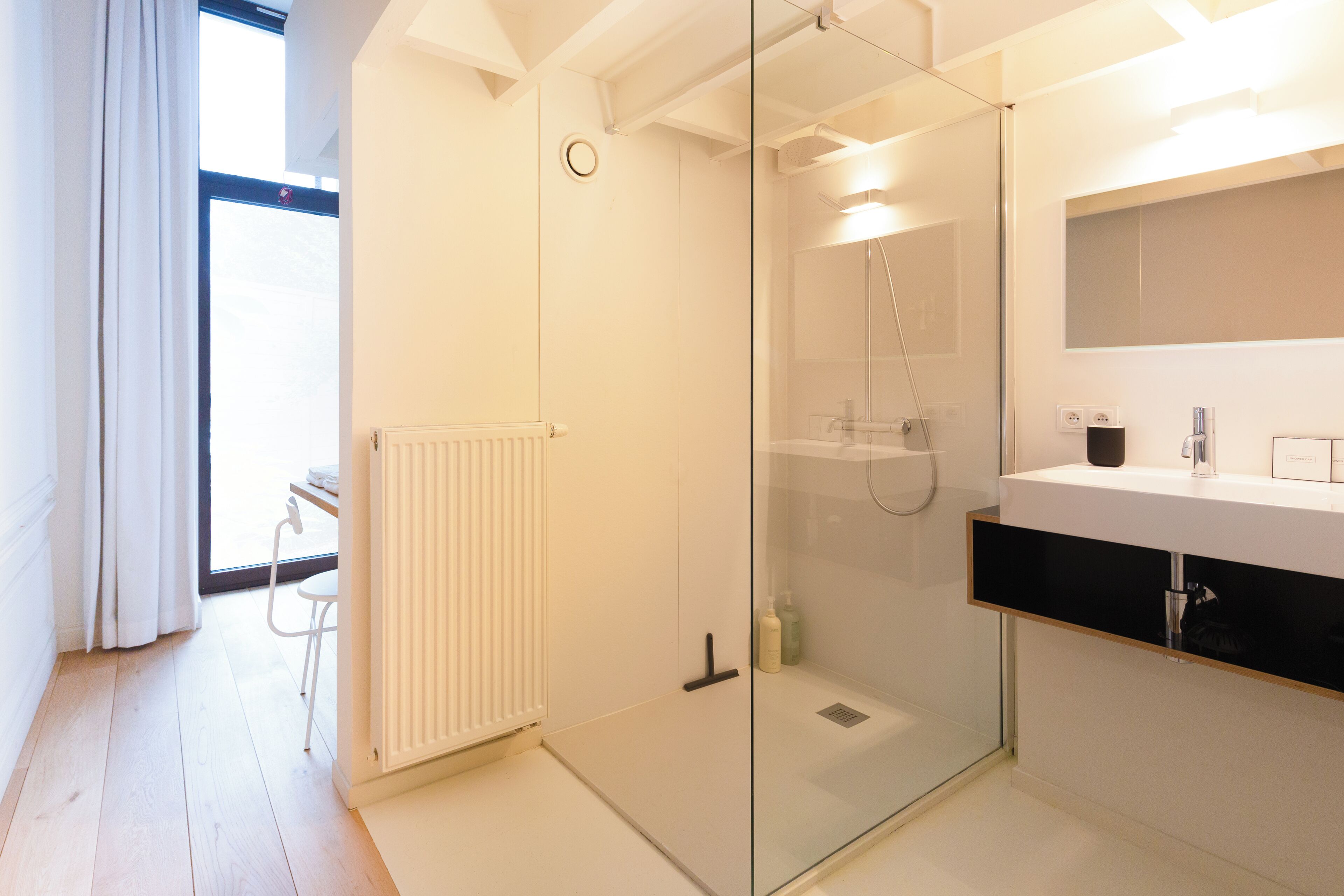 Un baño moderno con cabina de ducha de vidrio, un lavabo blanco con encimera negra y un radiador en el suelo.