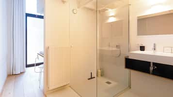 Un baño moderno con cabina de ducha de vidrio, un lavabo blanco con encimera negra y un radiador en el suelo.