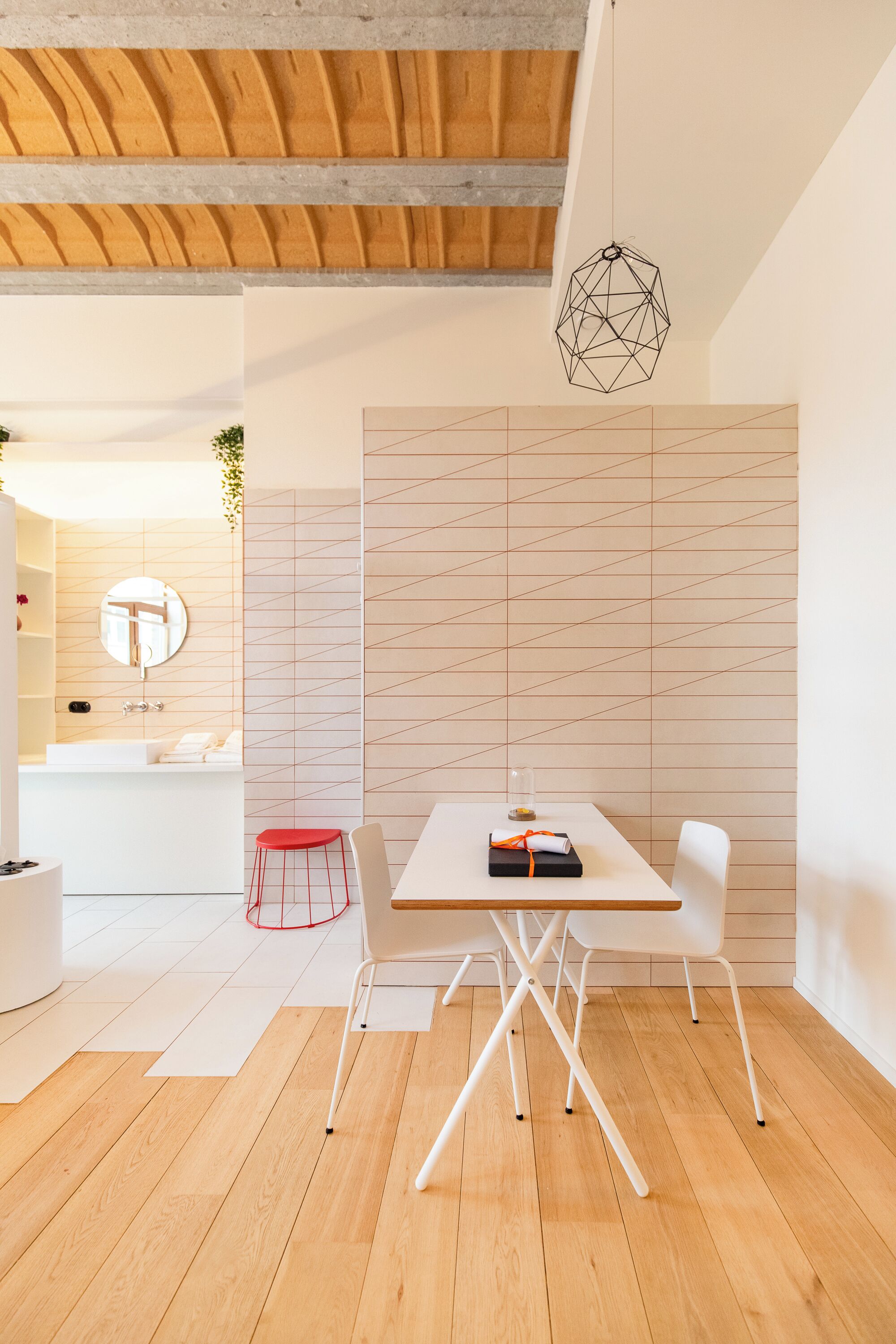 A modern interior with a wooden ceiling, a white table with chairs, a geometric light fixture, and a patterned wall.