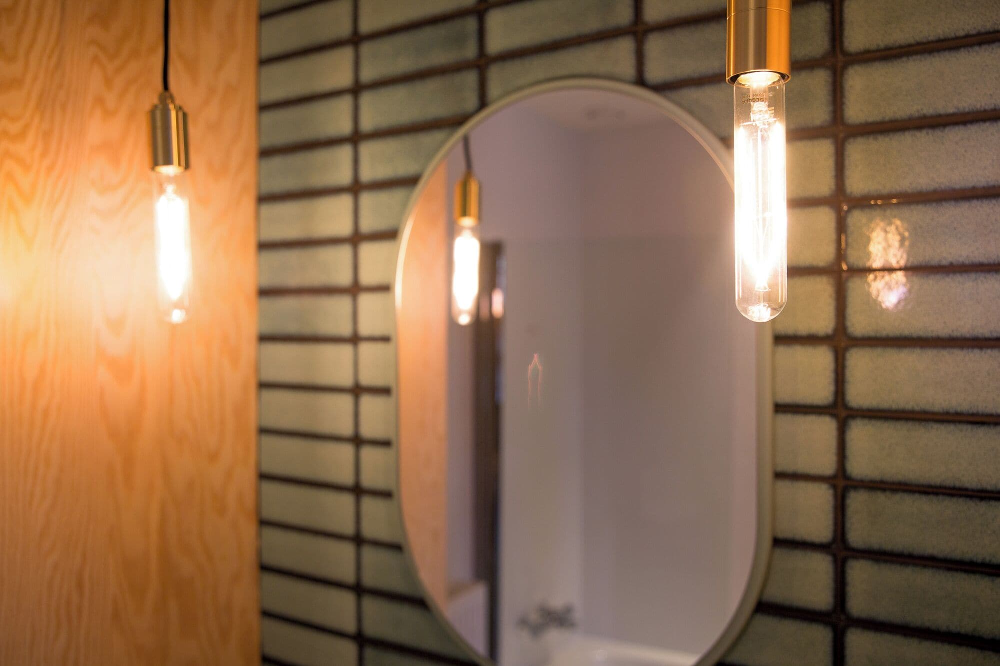 Un baño con espejo, pared de madera y lámparas colgantes.