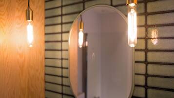 Un baño con espejo, pared de madera y lámparas colgantes.