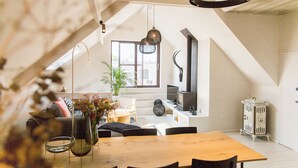 A modern loft with a high ceiling, exposed beams, a wooden dining table, and a large window providing natural light. - The Hide (Ghent)