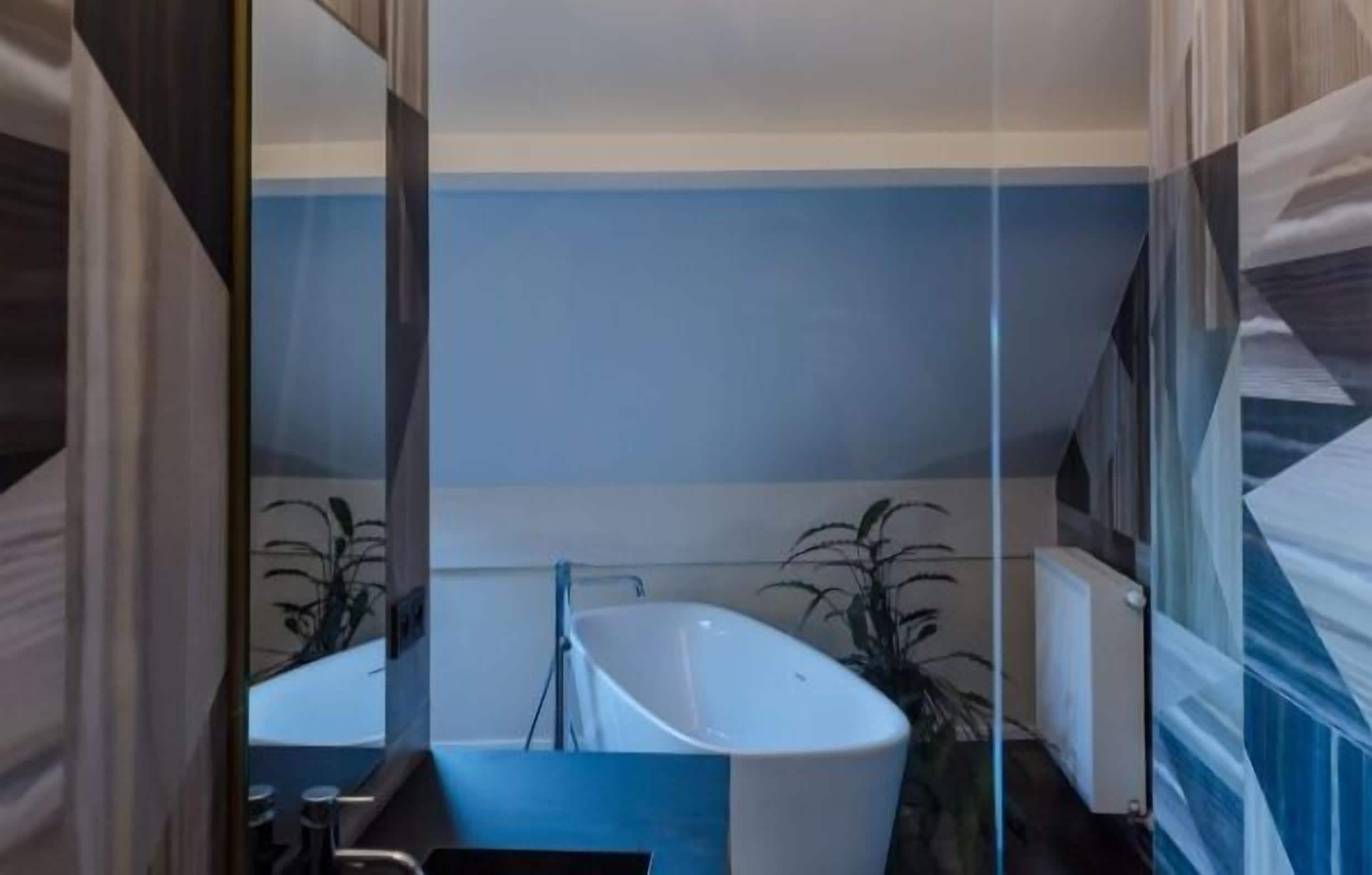 Une salle de bain moderne avec une baignoire sur pieds, un miroir et deux plantes en pot.