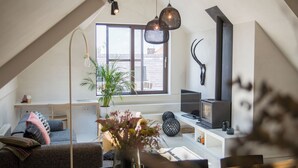 A modern loft with a sloped ceiling, a large window, a fireplace, and a cozy seating area with a sofa and a coffee table. - The Hide (Ghent)