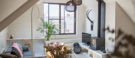 A modern loft with a sloped ceiling, a large window, a fireplace, and a cozy seating area with a sofa and a coffee table.