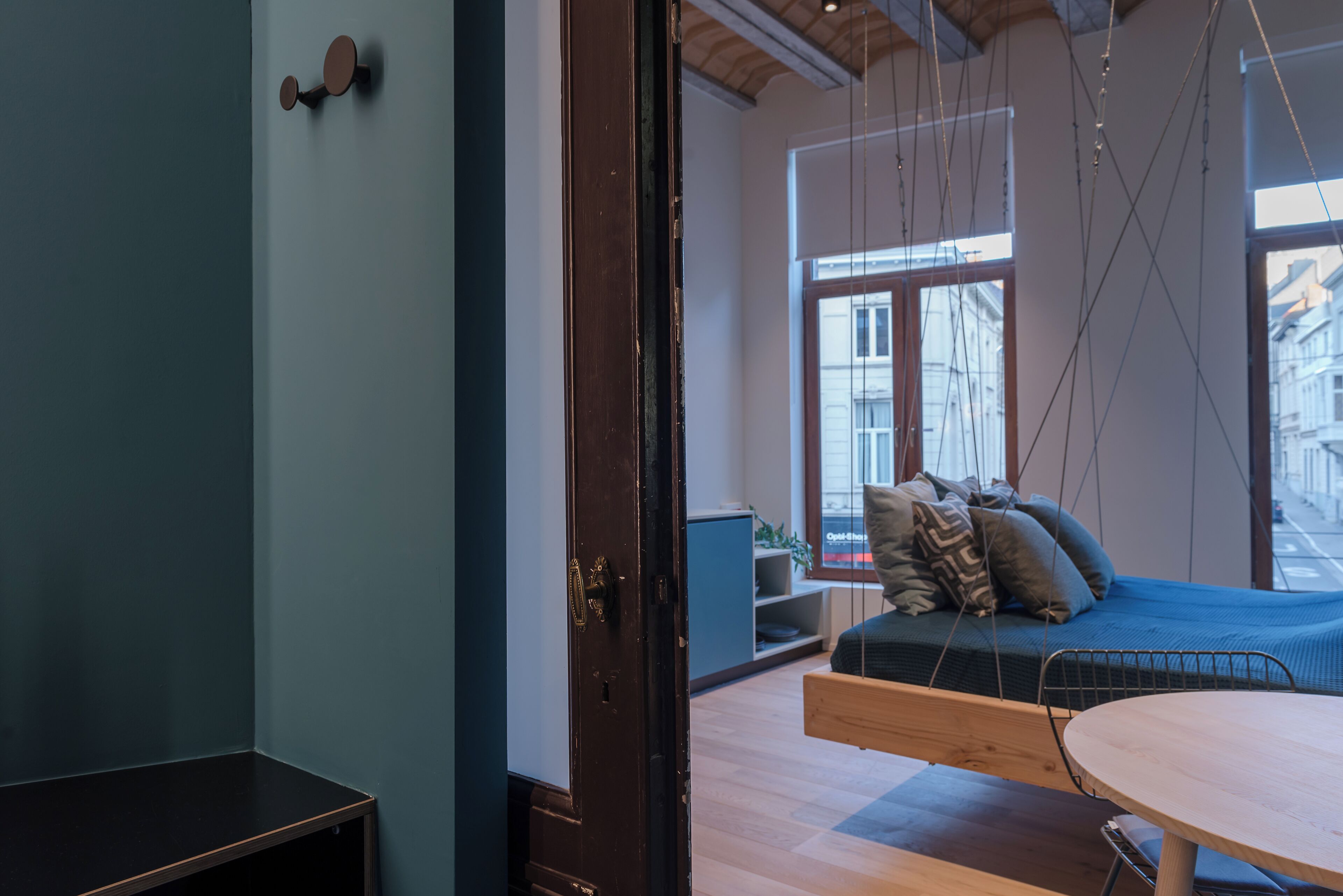 Una habitación con una cama colgante, una mesa de madera y vistas a la ciudad a través de amplias ventanas.