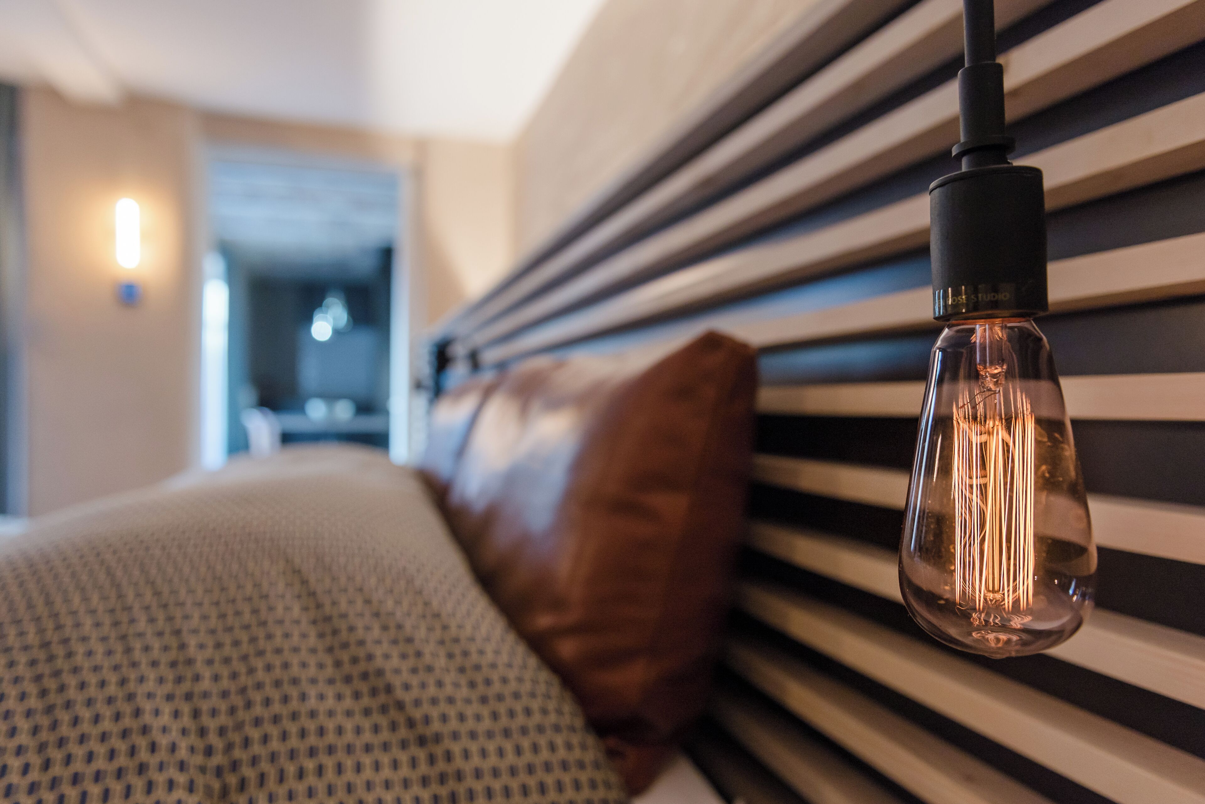 A bed with a striped headboard, a hanging light fixture, and a visible door in the background.