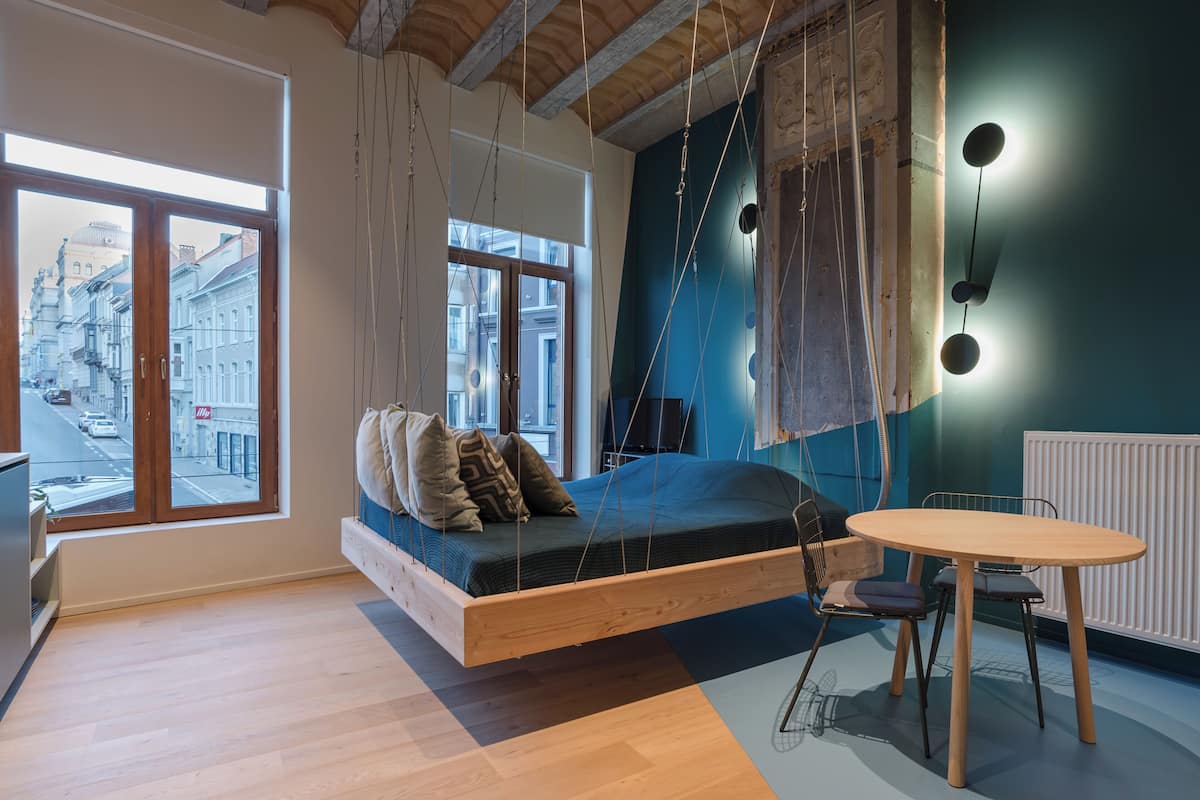 A modern room with a hanging bed, a round table, and large windows offering a city view.