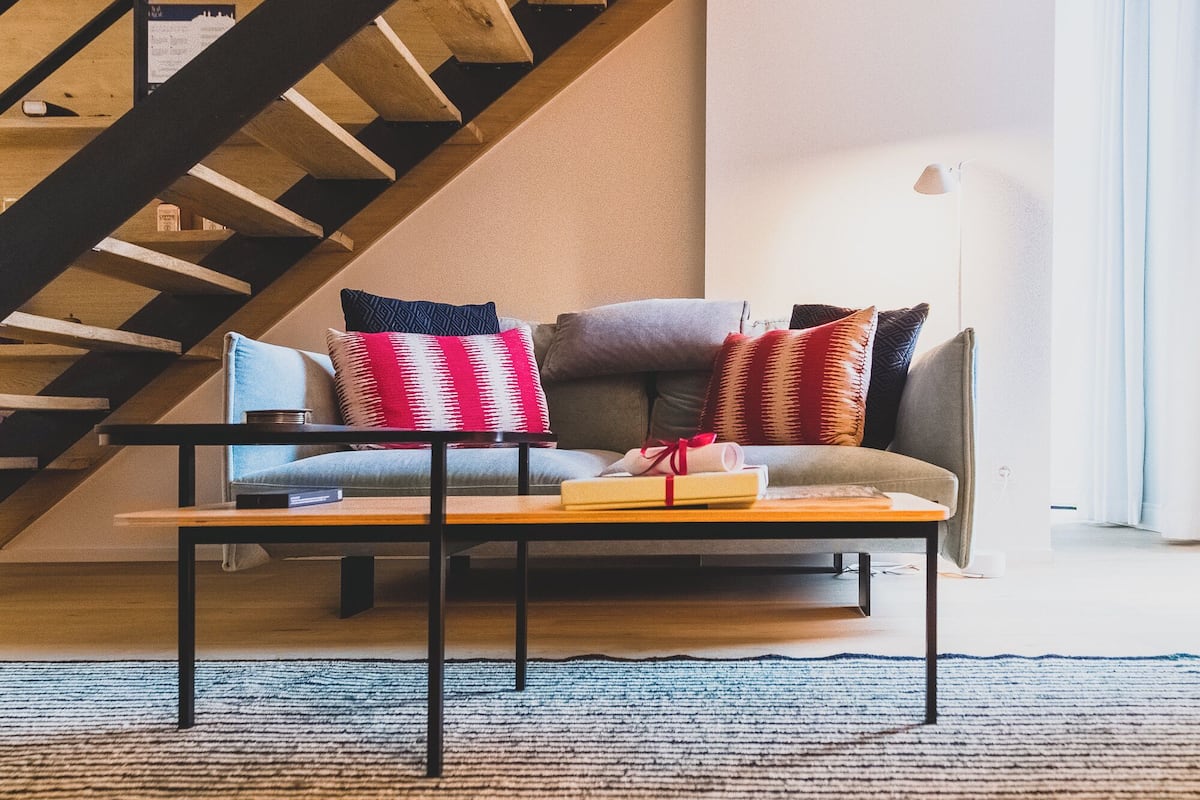 A modern interior with a wooden staircase, a sofa with cushions, and a patterned ceiling.