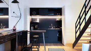 A compact kitchen with dark cabinetry, a bar stool, and a modern pendant light.