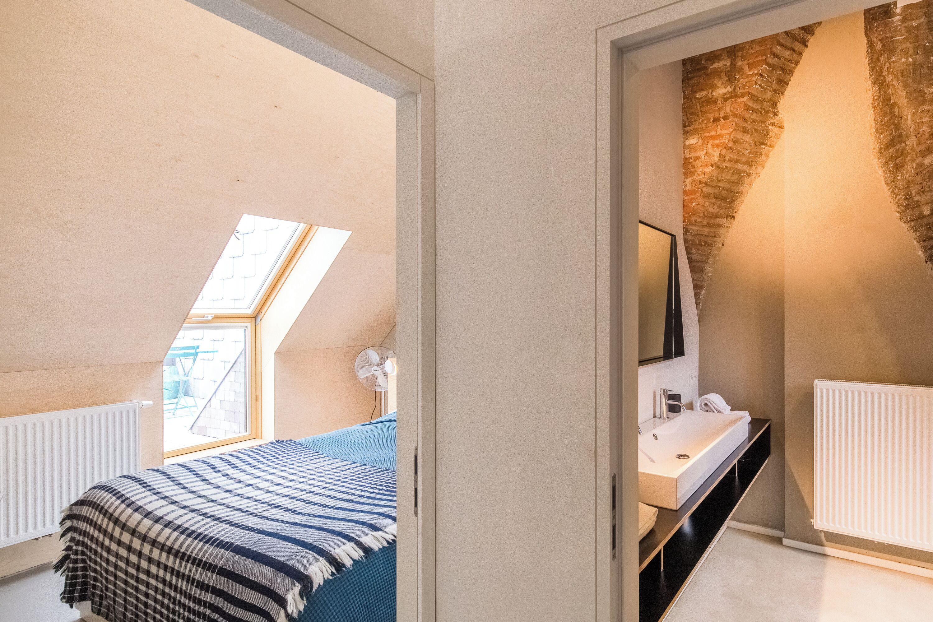 A bedroom with a skylight, a bed with a striped blanket, a bedside table, and a white radiator.
