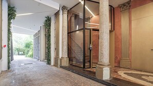 A corridor with patterned flooring, columns, and a glass door leading to a staircase. - The Hide (Ghent)