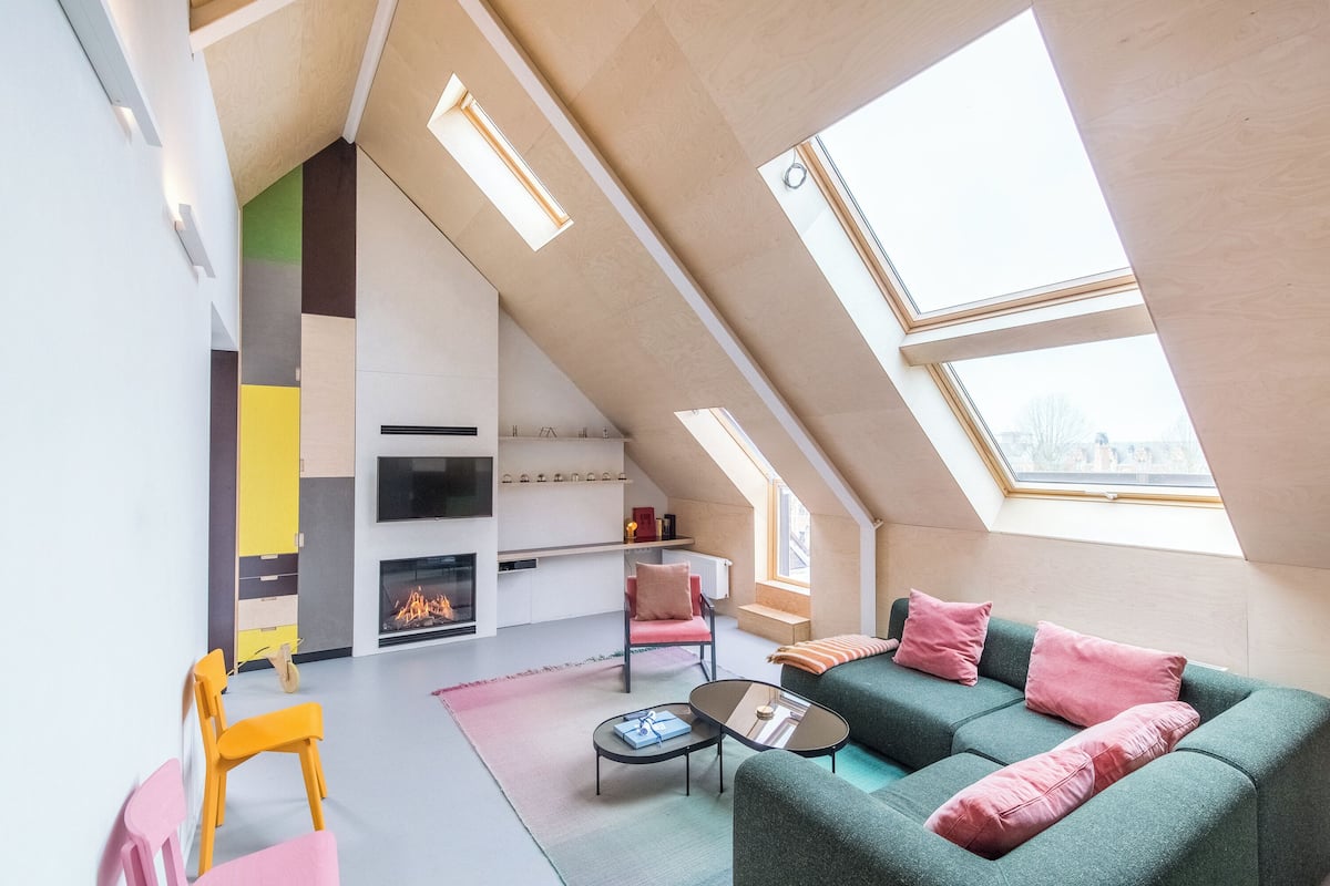 A modern loft-style living room with a sloped ceiling, built-in seating, a fireplace, and skylights.