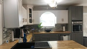 Una cocina con armarios blancos, un lavamanos negro, una estufa y una ventana con vistas a edificios.