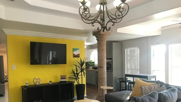 Una sala de estar con un sofá gris, una pared de acento amarilla y un televisor de pantalla plana.