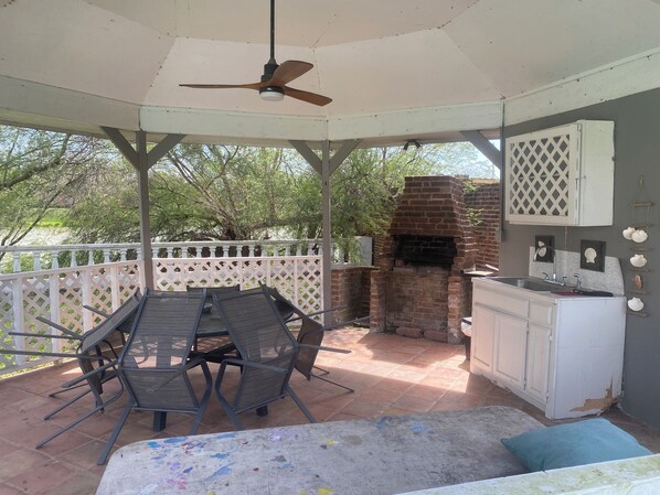 A covered patio with a brick oven, outdoor seating, and a white fence.