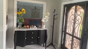 Una habitación de esquina con un escritorio negro, un espejo, un jarrón con flores y un perchero.