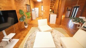 Un intérieur en bois avec un téléviseur, des canapés blancs, une petite cuisine et un escalier.