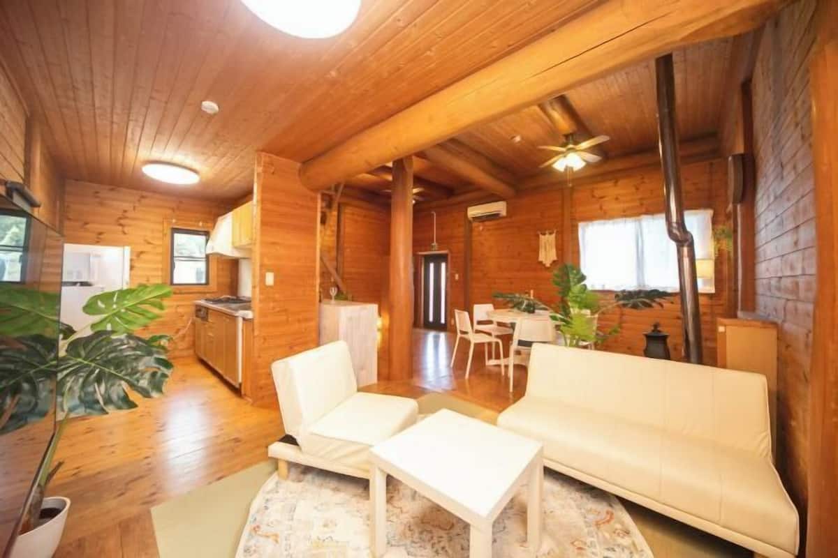 A cozy log cabin interior with a sofa, chairs, a dining table, and a kitchen area.