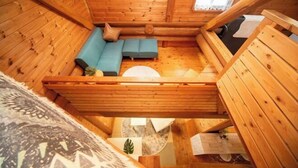 L’intérieur d’une cabane en rondins, avec un lit en mezzanine, un canapé et une petite fenêtre.