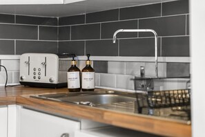 A kitchen with a white toaster, two bottles of hand and dish soap, a stainless steel sink, and a black dish rack.