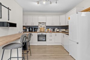 A modern kitchen with white cabinets, a wooden countertop, a built-in oven, and a refrigerator.