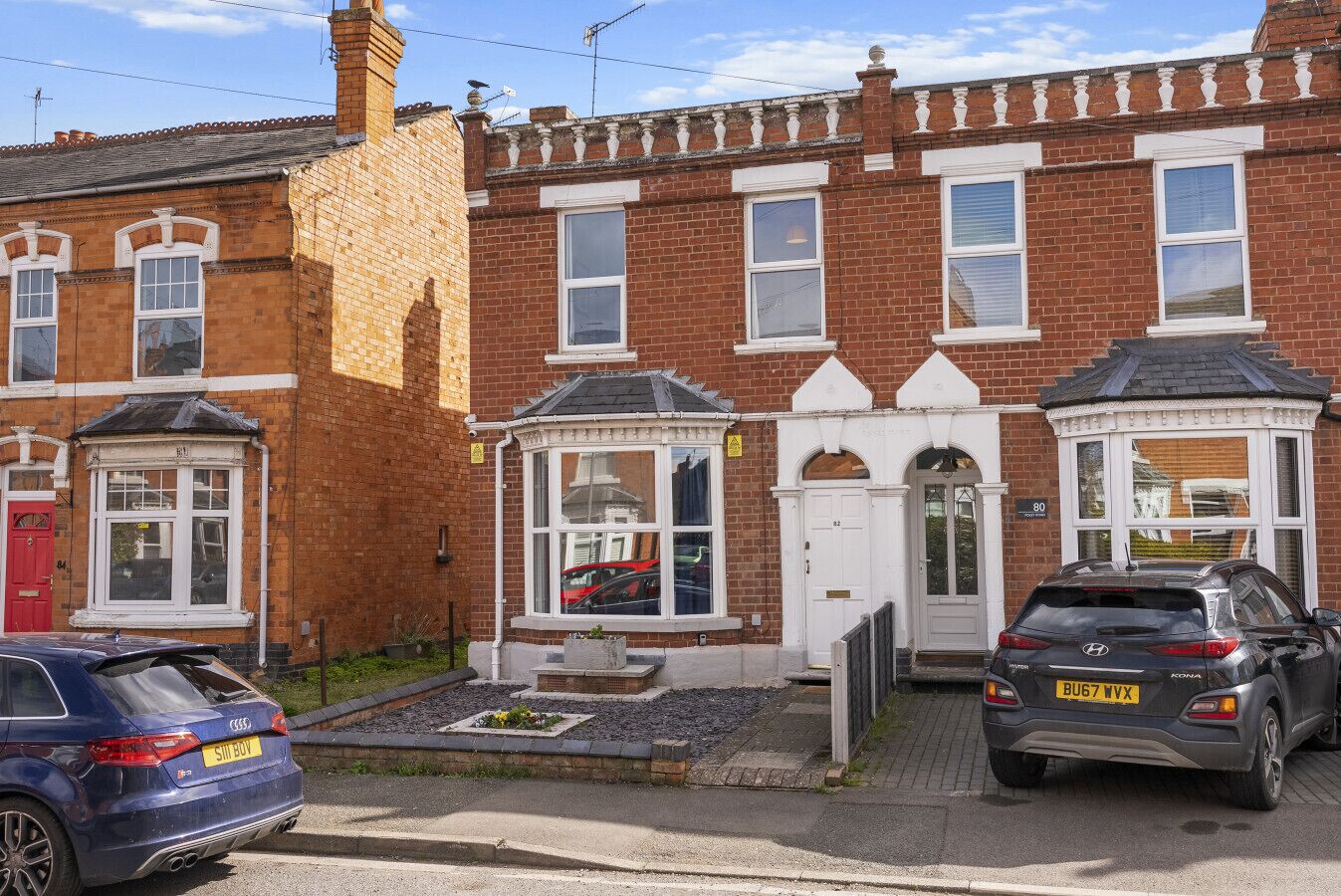 A row of terraced houses with a front garden, a red door, and a parked car.