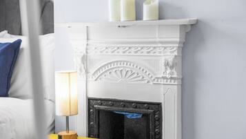 A white fireplace with three candles, a blue pillow, and a yellow nightstand with a lamp.