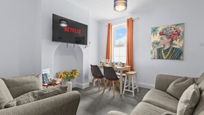 A living room with a flat-screen TV, a dining table with chairs, a sofa, and a painting on the wall. - Charming 5-Bed Victorian House (Worcestershire)