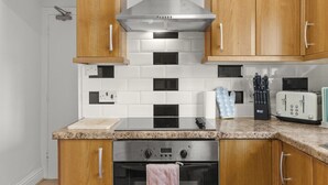A kitchen with wooden cabinets, a stainless steel range hood, a built-in oven, and a toaster. - Charming 5-Bed Victorian House (Worcestershire)
