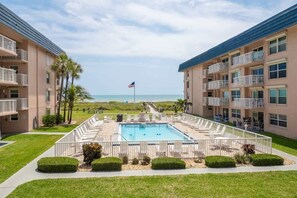A pool area with a view of the beach, surrounded by apartment buildings. - Ocean View Balcony | Heated Pool | Rocket Launch Views | 2B/2Ba (Cocoa Beach)