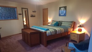 Un dormitorio con una cama, mesitas de noche, una silla, una pequeña mesa con una planta y un cubo de basura.