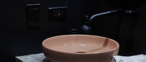 Een badkamer met een rond, bruin wastafel op een donker aanrecht, een handdoek en een spiegel.