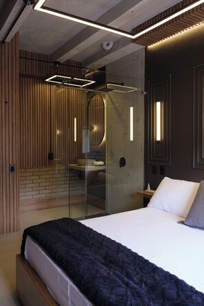 A modern bedroom with a large bed, a glass shower enclosure, and a wooden wall paneling. - Bindi Hostel (Salento)