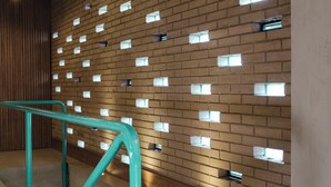 Un intérieur moderne avec un mur de briques agrémenté de petites fenêtres carrées, une rambarde de couleur turquoise et un sol en béton.