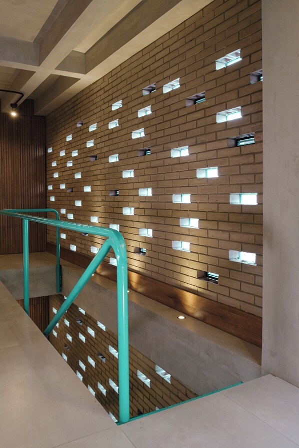 A modern interior with a brick wall featuring small square windows, a teal handrail, and a concrete floor.