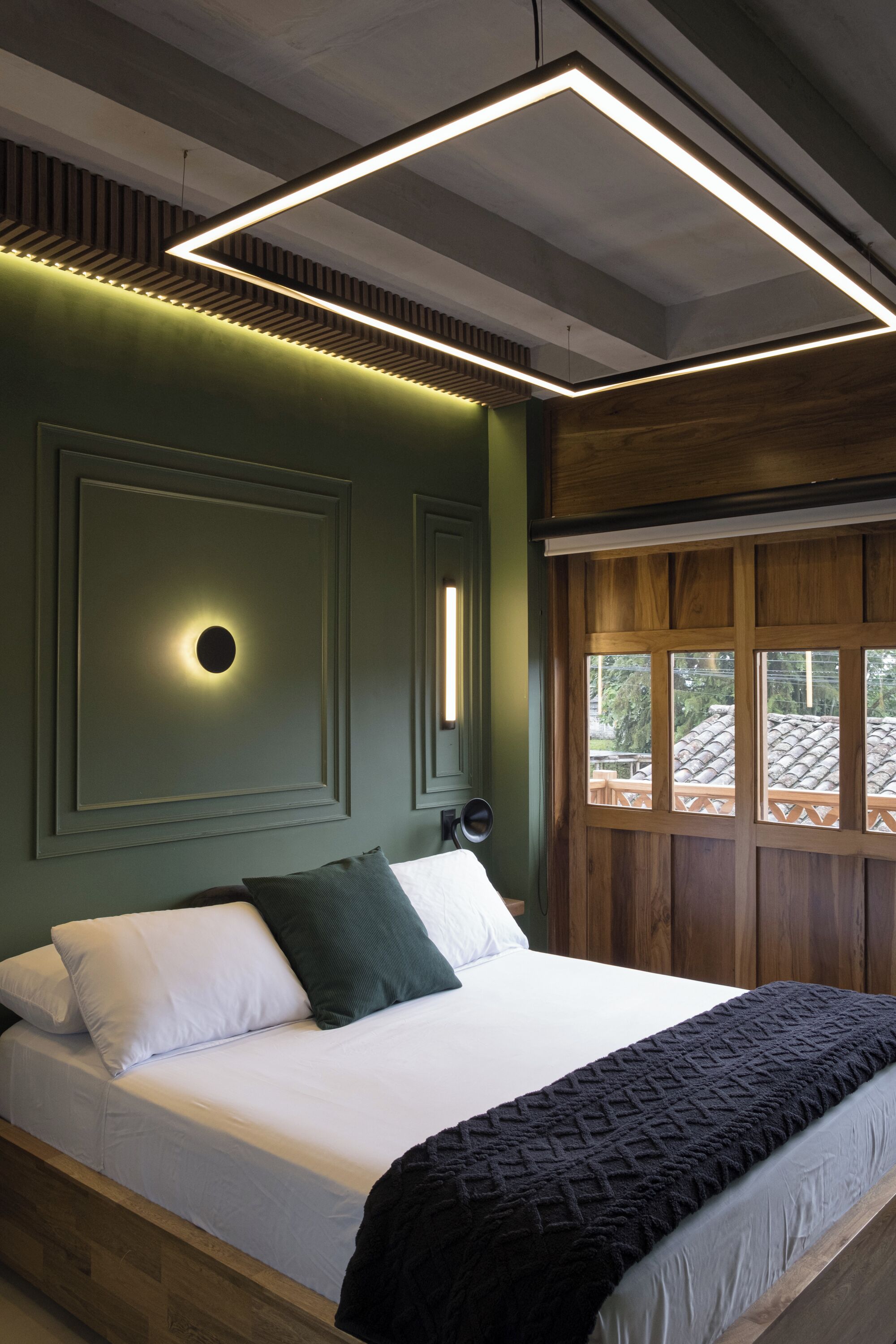 A bedroom with a bed, a window, and a wall-mounted light fixture.