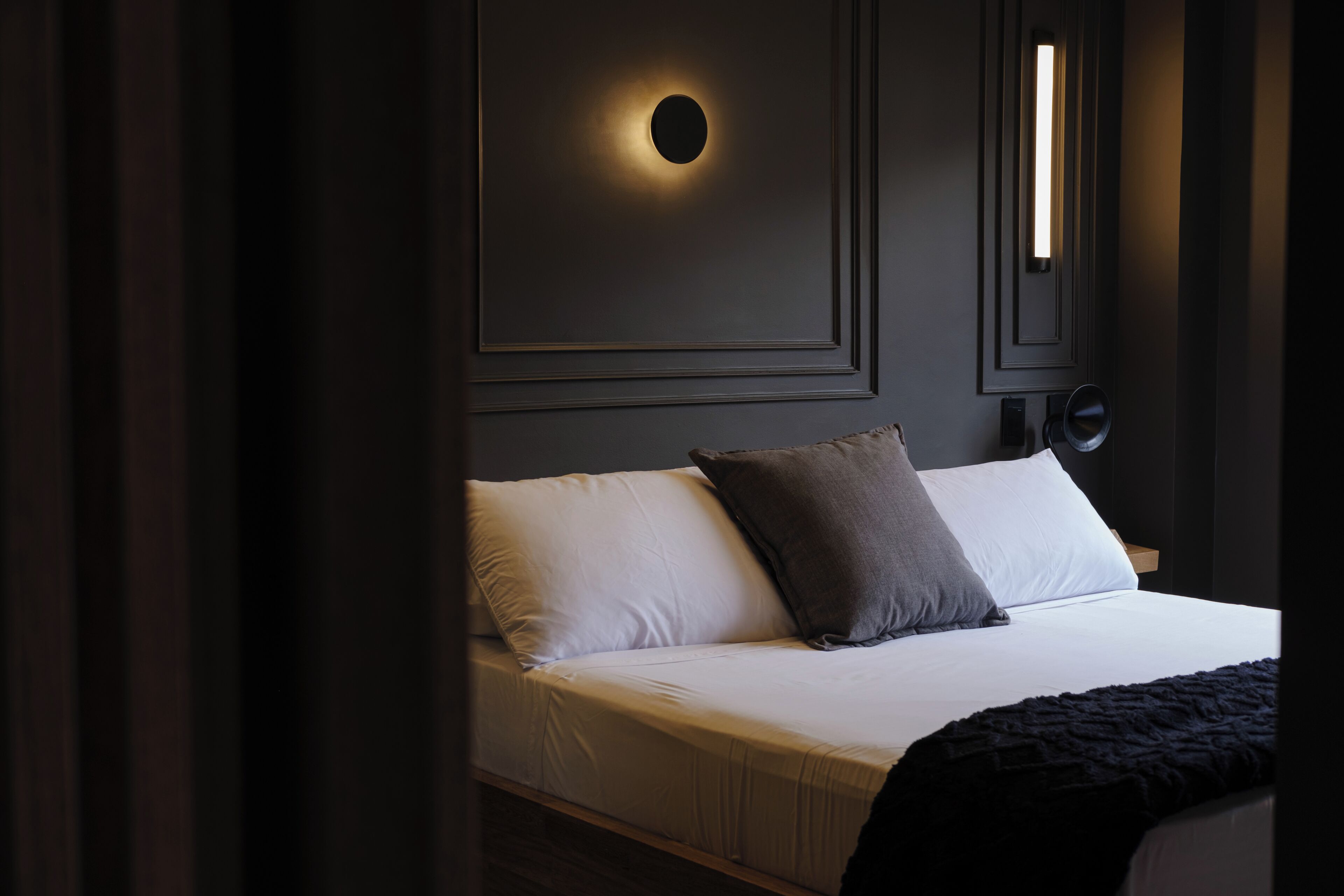 A bedroom with a bed, pillows, and a wall-mounted light fixture.
