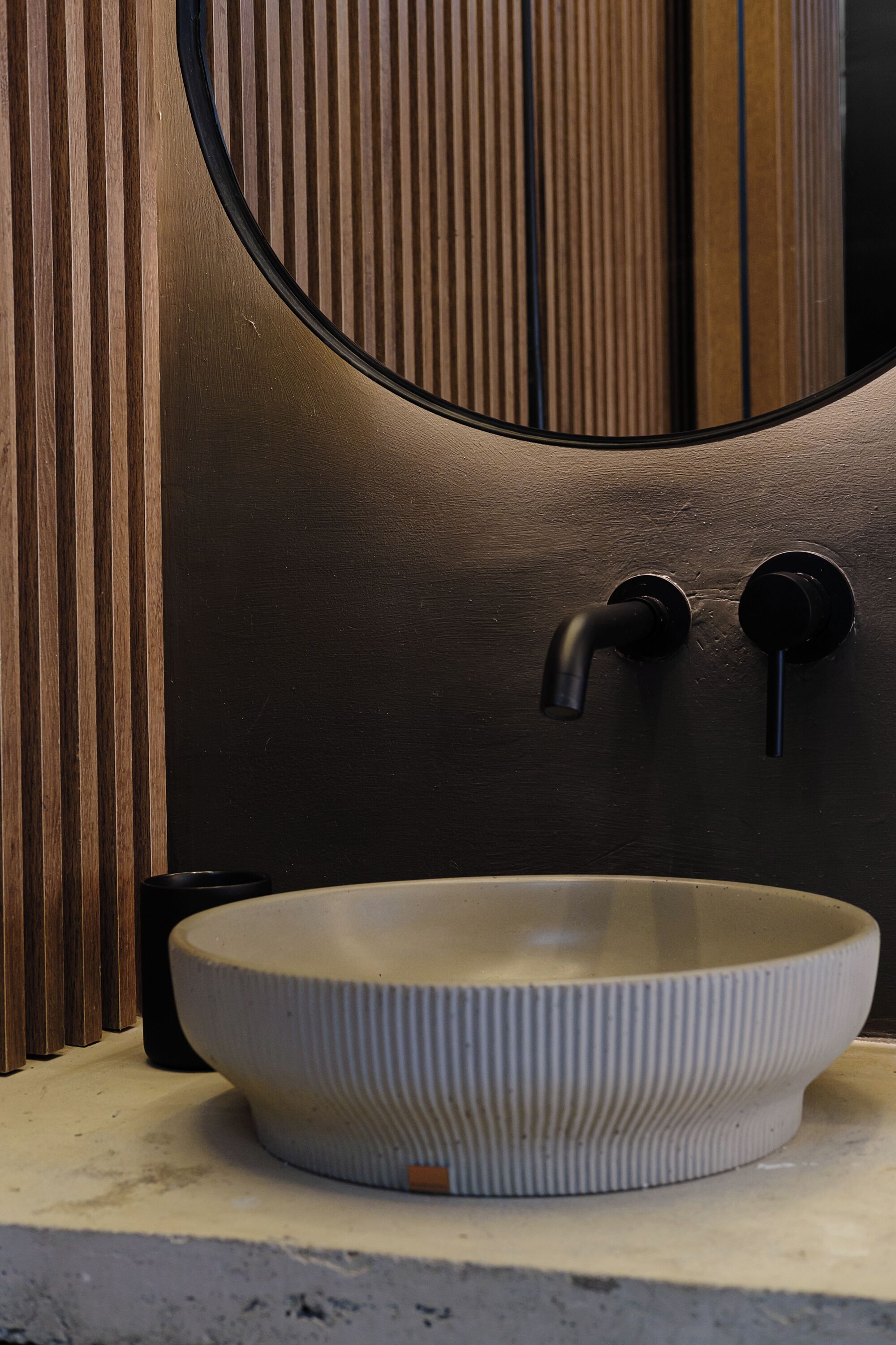 A modern bathroom with a round mirror, a white ribbed sink, and wooden paneling.