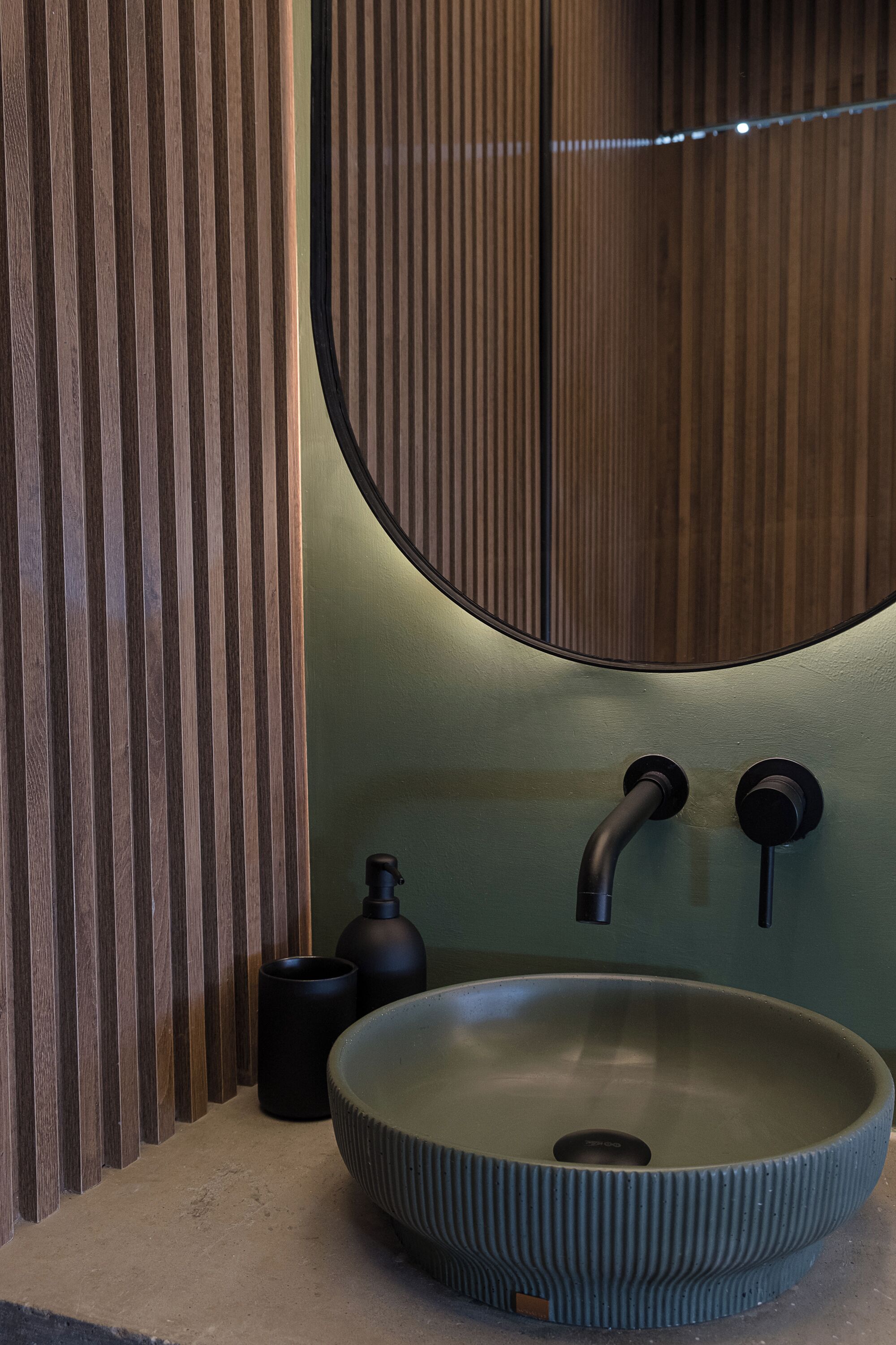 A modern bathroom with a round vessel sink, a mirror, and vertical wooden slats.