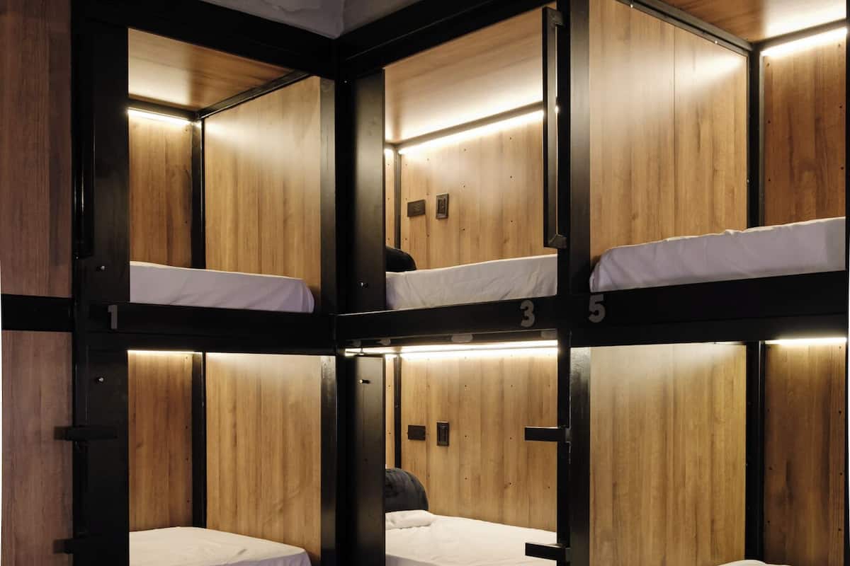 A bunk bed room with wooden walls and metal frames, featuring multiple beds and a small seating area.