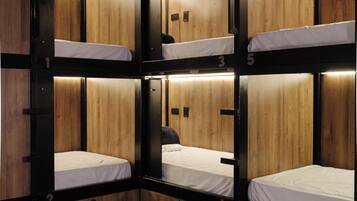 A bunk bed room with wooden walls and metal frames, featuring multiple beds and a small seating area.