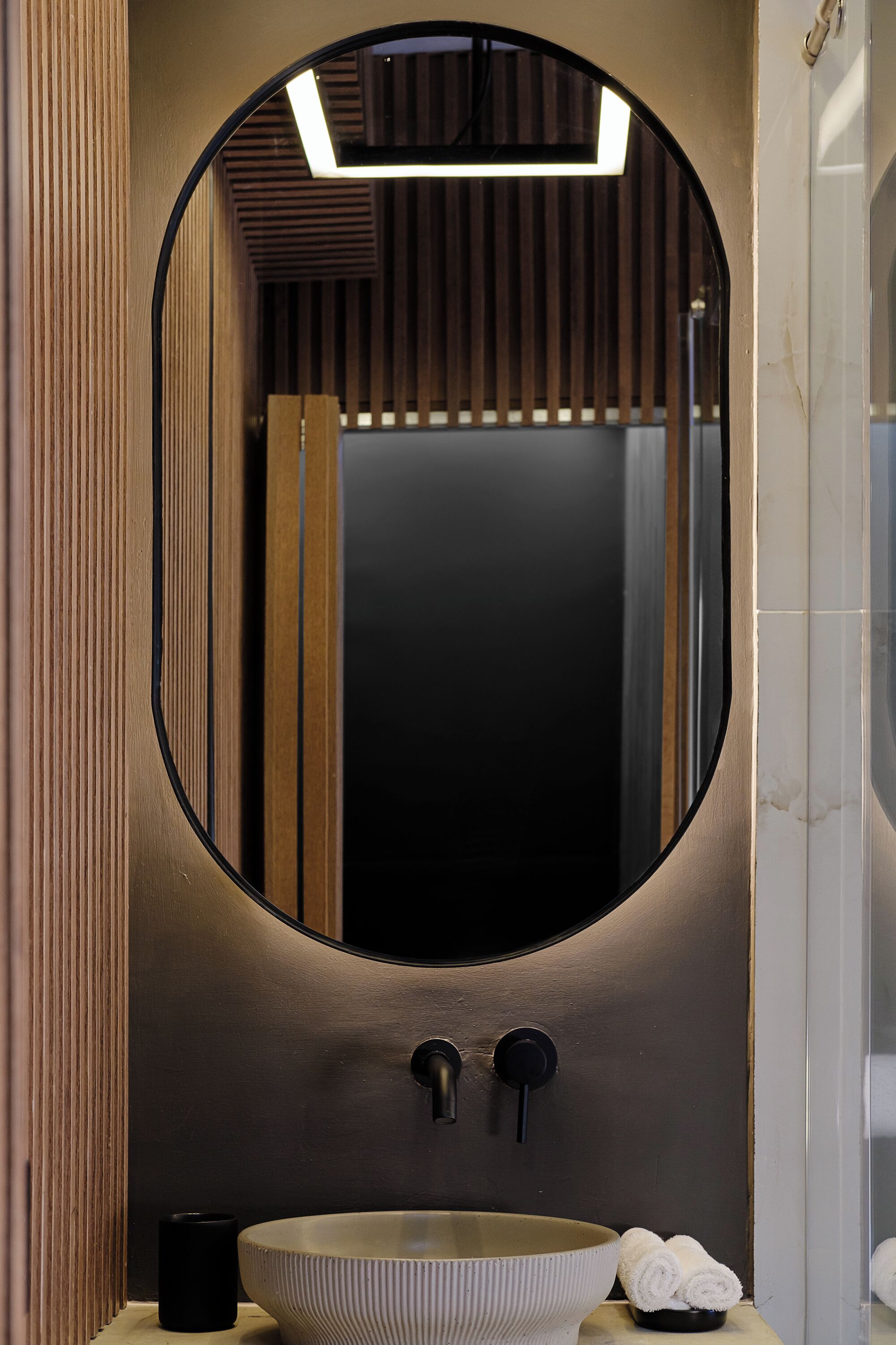 A bathroom with a round mirror, a sink, and a towel rack.