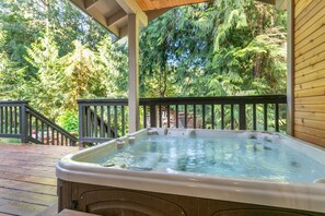 A hot tub on a wooden deck with a railing, surrounded by trees. - Mt. Baker Cabin | Hot Tub | Fiber Internet | Generator (Deming)