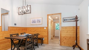 A wooden-paneled room with a dining table, chairs, a bench, a coat rack, and a hallway leading to another room.